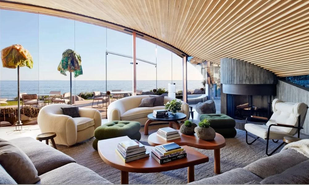 Spacious oceanfront living room with curved sofas, lounge chairs, and ottomans arranged around coffee tables